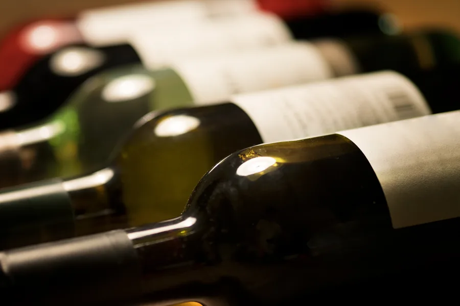 Botellas de vino tumbadas en una bodega, con sus etiquetas de papel blanco
