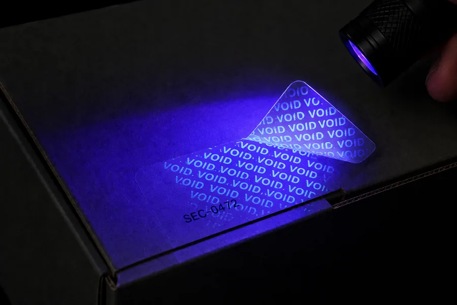 Precinto transparente despegado que revela un motivo VOID luminiscente bajo una linterna UV